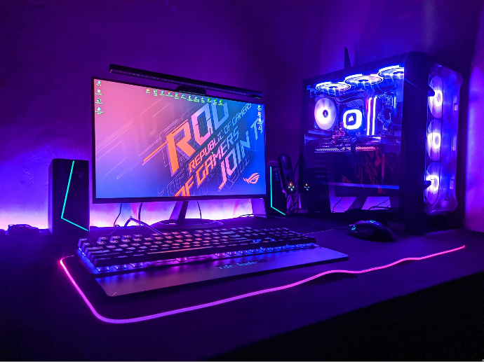 Un setup d'ordinateur de jeu avec un moniteur, un clavier et une tour dans une lumière violette